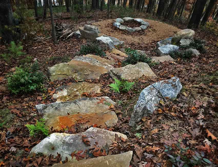A stone path in a wooded area with a fire pit.