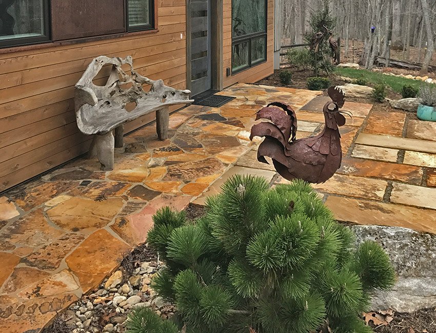 A stone patio with a rooster statue in front of it.