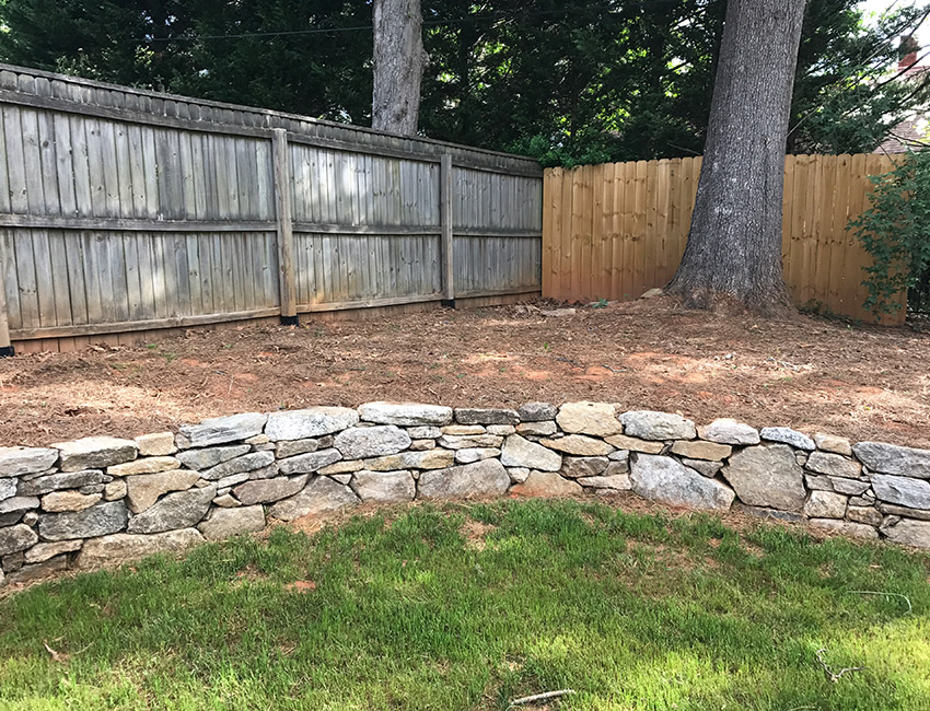 A backyard with a stone wall and a fence.