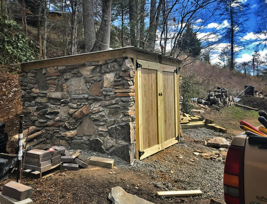 A stone shed is being built in a wooded area.