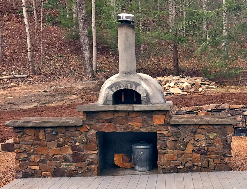 An outdoor pizza oven sitting on a wooden deck.