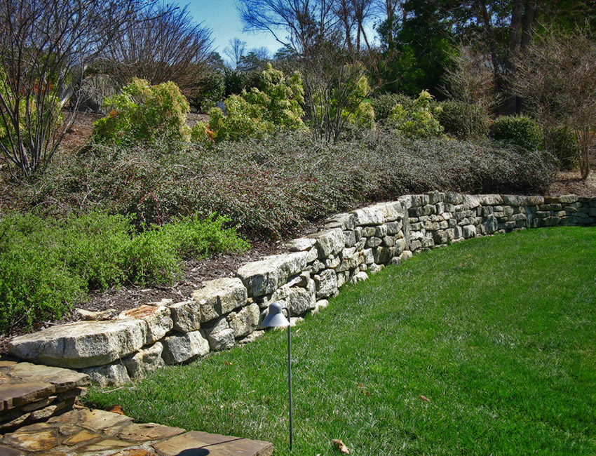 A stone wall surrounded by grass and shrubs.